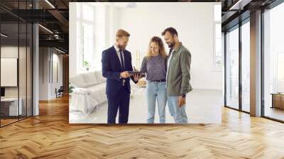 Happy couple signs lease or purchase agreement after inspecting house at meeting with realtor. Excited woman puts her signature while standing with her husband in living room of her new home. Wall mural