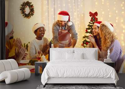 Happy diverse friends sit at table eating delicious Christmas food celebrate winter holidays together. Smiling multiracial young people enjoy meal at New Year domestic celebration. Home party. Wall mural