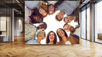 Happy diverse team having fun together. Low angle group portrait of cheerful joyful young and senior Caucasian and African American business people friends huddling, looking down at camera and smiling Wall mural