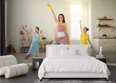 Happy family having fun while cleaning their house. Cute little children helping mom tidy up their apartment. Smiling young mother and daughters dancing together while mopping the floor at home Wall mural