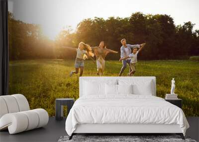 Happy family playing and having fun in nature. Cheerful, joyful mum, dad and children running together on a grassy lawn in a beautiful, fresh, green park on a warm, sunny summer evening Wall mural