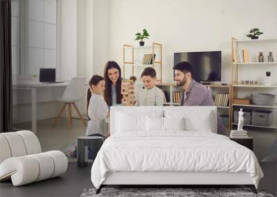 Happy family with kids playing board games at home. Smiling mom, dad and children sitting on the floor around a low table in a cozy living room and pulling wooden blocks from the tower Wall mural