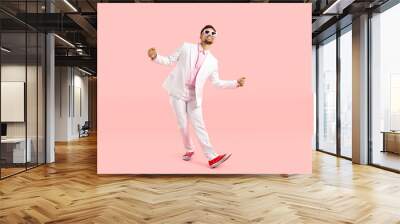 Happy funny guy in white suit dancing isolated on pastel pink background. Full body shot of cheerful goofy carefree man in modern suit, sneakers and glasses dancing and having fun in the studio Wall mural