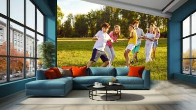 Happy kids playing games and having fun in summer camp on vacation. Team of children playing tug of war, standing on green field and pulling rope all together. Summer, fun, activity, teamwork concept Wall mural