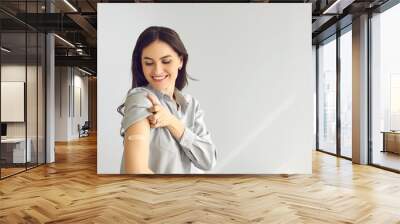 Happy lady shows bandage on her arm after getting flu or Covid-19 vaccine. Woman promoting coronavirus vaccination and immunization campaign on light gray empty blank text copyspace studio background Wall mural