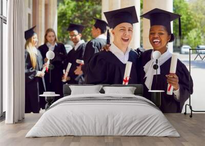 Happy smiling caucasian man afroamerican woman in graduation gown and cap graduate universuty with group of students on background looking at camera. Graduation from high school, college, university. Wall mural