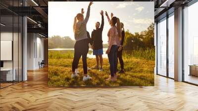 Happy smiling sporty group of people jumping standing in a circle in nature with hands up rejoicing the success in sport training or exercise achievement outdoors after workout in the park. Wall mural