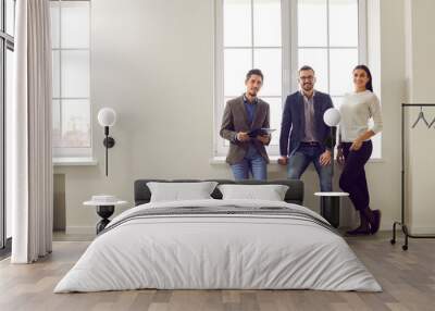 Happy to work with professionals. Portrait of a happy, successful business team in the office. Group of three smiling young people standing together by an office window Wall mural