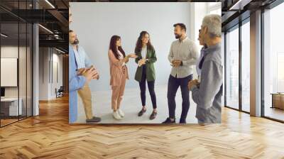 Happy young and mature people having friendly conversation at business event. Group of men and women meeting with business coach. Team of employees standing in office and having interesting discussion Wall mural