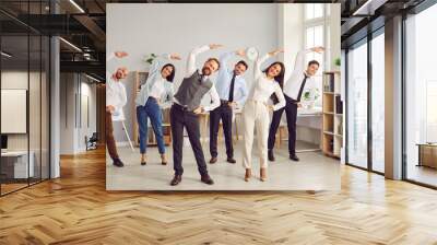 Happy young business people doing stretching sport exercises standing together in modern office. Group of smiling company employees exercising fitness for health during a break from a work. Wall mural