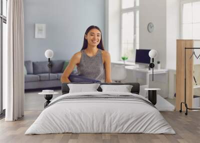 Happy young girl with yoga mat in hand leaning on her office desk getting ready to hit the gym Wall mural