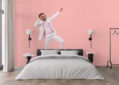 Happy young man in stylish pink shirt, white summer suit and sunglasses dancing isolated on solid pastel pink color copy space background. Partying and having fun concept Wall mural