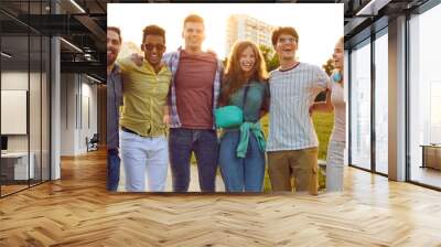 Happy young people enjoying summer, spending time outdoors and having fun together. Joyful excited diverse friends standing in the city park, hugging each other and smiling. Group portrait. Banner Wall mural