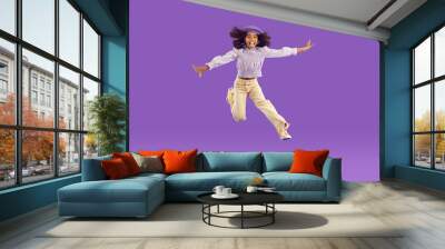 Hooray. Happy joyful kid girl in comfortable trendy wear jumping high. Full length portrait African child with curly hair, in funky pants and beret hat feeling free, overjoyed, excited and having fun Wall mural