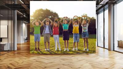 Kids having fun in summer park. Full body length group shot of happy, cheerful children, standing on green lawn or camp field in warm sunlight, raising hands up and doing heart gestures. Love concept Wall mural