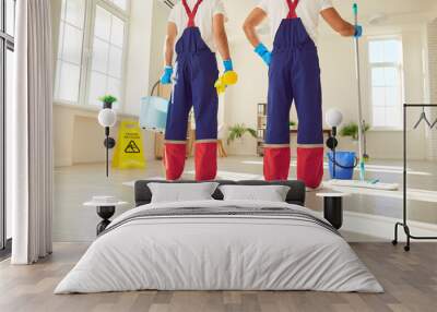 Legs of a team of professional janitors in uniform going to wash the floor with detergent at home or at office. Male cleaners with mop standing in client house indoors. Cleaning service concept. Wall mural