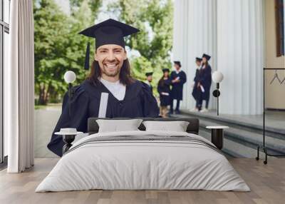 Male graduate is smiling against the background of university graduates. Wall mural