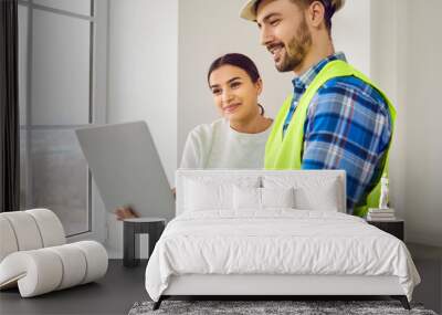 Man builder, architect or construction worker in a hardhat and uniform workwear meeting with a happy young woman and showing her a house building plan on a modern laptop computer Wall mural