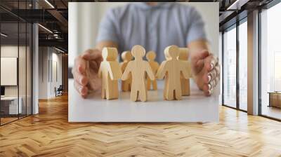 Man guarding little human figures on table. Close up of male hands protecting small pawn people on white desk. Responsible manager cares for his team and creates safe work community. Safety concept Wall mural