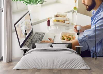 Man having takeaway meal and signing up for food delivery website during lunch break in office Wall mural