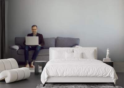 Mature businessman sitting on sofa working with laptop. Executive middle aged casually dressed man working in office lounge. Successful man working online via computer Wall mural