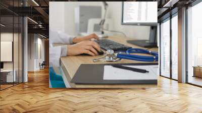 Medicine doctor's working table. Doctor's workspace working at computer and typing electronic medical record sitting near stethoscope and clipboard. Medicine concept. Focus on stethoscope. Close up. Wall mural