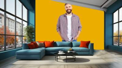 Men's casual style. Portrait of handsome smiling Caucasian young man in stylish comfortable casual clothes. Bearded man in jeans, t-shirt and shirt smiling looking at camera on orange background. Wall mural