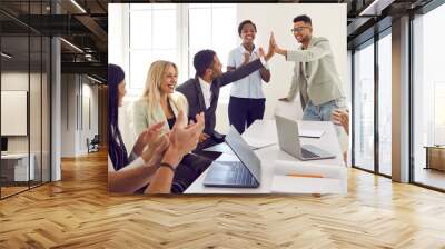 Mixed race business team celebrating good results in office meeting. Happy young black man gives high five to coworker while diverse multi ethnic teammates are applauding. Teamwork and success concept Wall mural