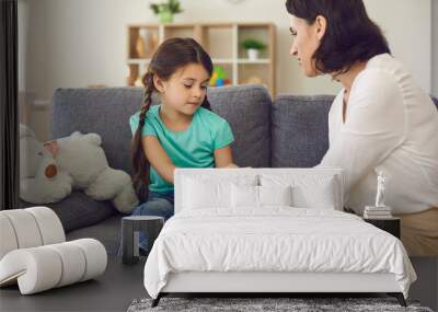 Mother sitting with daughter, holding her hands, talking to her and teaching her something Wall mural