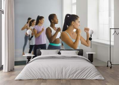 Multiethnic group of confident beautiful young ladies doing active sports workout at fitness studio. Team of strong multiracial women doing fighting move during physical training session at modern gym Wall mural