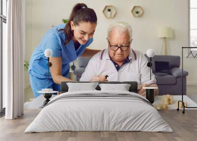 Nurse in geriatric clinic or retirement home helping patient with alphabet puzzle. Senior man sitting at desk and playing games with letters. Old age, dementia, Alzheimer's disease, therapy concept Wall mural