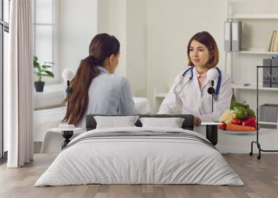 Nutrition expert talking to client about health problems and importance of eating healthy food. Doctor, nutritionist or dietitian discussing treatment with young woman and making individual diet plan Wall mural