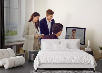 Online communication. Business team having video call meeting with colleague. Three happy young people gather at office table with modern computer and have discussion with remote colleague Wall mural