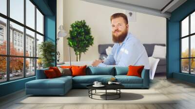 Online work at home. A serious fat bearded man is looking at the camera in the workplace at home. Wall mural