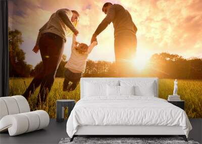 Parents hold the baby's hands.  Happy family in the park evening Wall mural