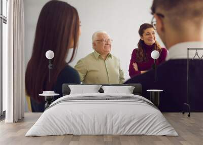 People of different ages gathering together and talking. Happy senior man smiling and laughing having conversation with young men and women in group therapy session or community club meeting Wall mural