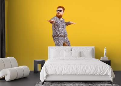 Plus size male model in funny PJs having fun in modern fashion studio. Happy carefree confident fat bearded man in comfortable leopard pajamas and cool glasses dancing isolated on yellow background Wall mural