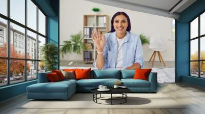 Portrait happy young woman business auditor accountant in casual shirt sitting at office desk with documents in front of camera, saying hello at online video call work meeting, waving hand and smiling Wall mural