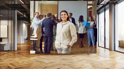 Portrait of a happy smiling confident young business woman looking at the camera with a team of company employees talking and working in the background in modern office after meeting. Wall mural