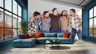 Portrait of a male mature bearded friends looking cheerful at each other and smiling on grey wall background. Photo of a group of brutal friendly men hugging and laughing in casual clothes. Wall mural