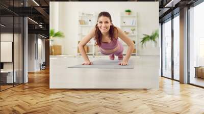 Portrait of a young attractive sporty woman doing push-up or plank sport exercises lying on yoga mat on the floor in the living room at home. Fitness, workout and home training concept. Wall mural