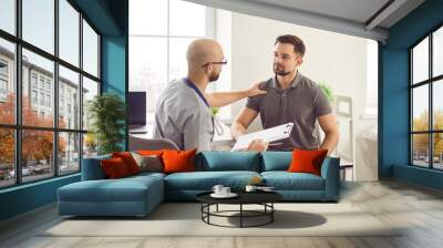 Portrait of a young man patient in medical office listening to a friendly doctor holding report file with appointment and giving consultation during medical examination in the clinic. Wall mural