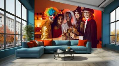 Portrait of cheerful happy multiracial adult friends with glasses of champagne at home party for Halloween. Smiling people in creepy costumes are clinking glasses in dark room and looking into camera. Wall mural