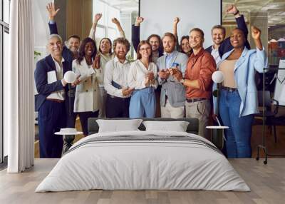 Portrait of diverse excited happy business people standing in office applauding and looking cheerful at the camera. Group of coworkers men and women smiling indoors. Team work concept. Wall mural