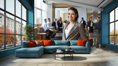 Portrait of happy female business teacher and professional coach. Beautiful young woman in jacket standing in office after corporate training class for team of employees, looking at camera and smiling Wall mural