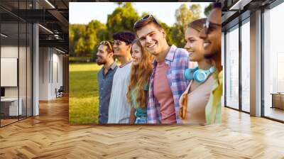 Portrait of joyful young man standing with his friends hanging out in public park. Cropped shot of group of cheerful multiracial friends gathered together in park on sunny summer day. Selective focus. Wall mural