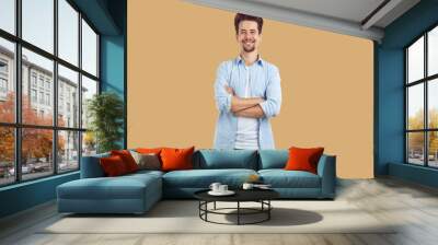 Portrait of smiling man standing with his arms folded. Handsome young man in casual clothing posing with crossed hands over isolated studio background with copy space Wall mural