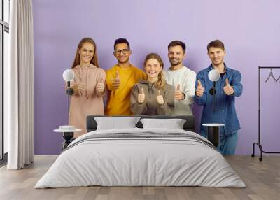 Portrait of smiling multiethnic young people isolated on violet background show thumbs up. Happy diverse multiracial teenagers recommend good training or internship. Recommendation concept. Wall mural