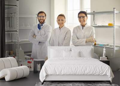 Portrait of smiling young scientist medical team wearing protective goggles, gloves and white coat in lab. Group of researchers in biotechnology laboratory standing and looking at camera Wall mural