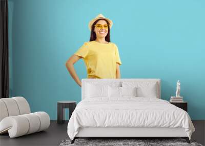 Portrait of young happy woman in casual summer clothes isolated on blue studio background. Smiling millennial girl in hat and sunglasses ready for summertime. Fashion and style concept. Wall mural